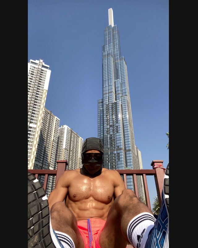 A masked athlete seated after outdoor training, photographed from a low angle against a high-rise skyline.