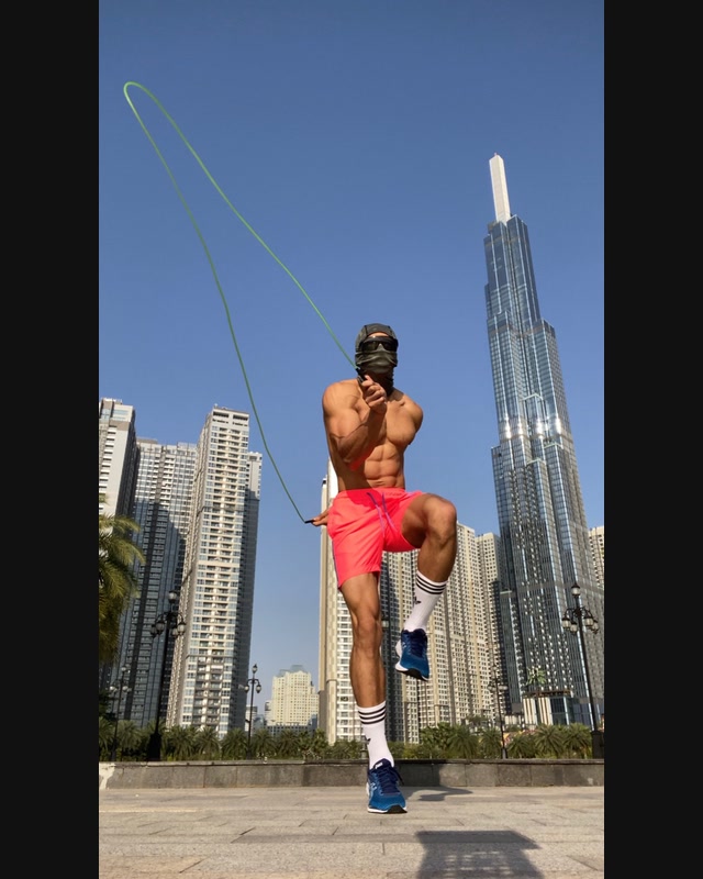 A masked athlete performs a jump-rope movement in an outdoor urban setting.